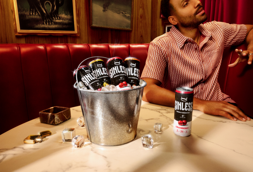 A man sitting in a booth and on the table in front of him is a bucket filled with ice and various flavors of Sinless.
