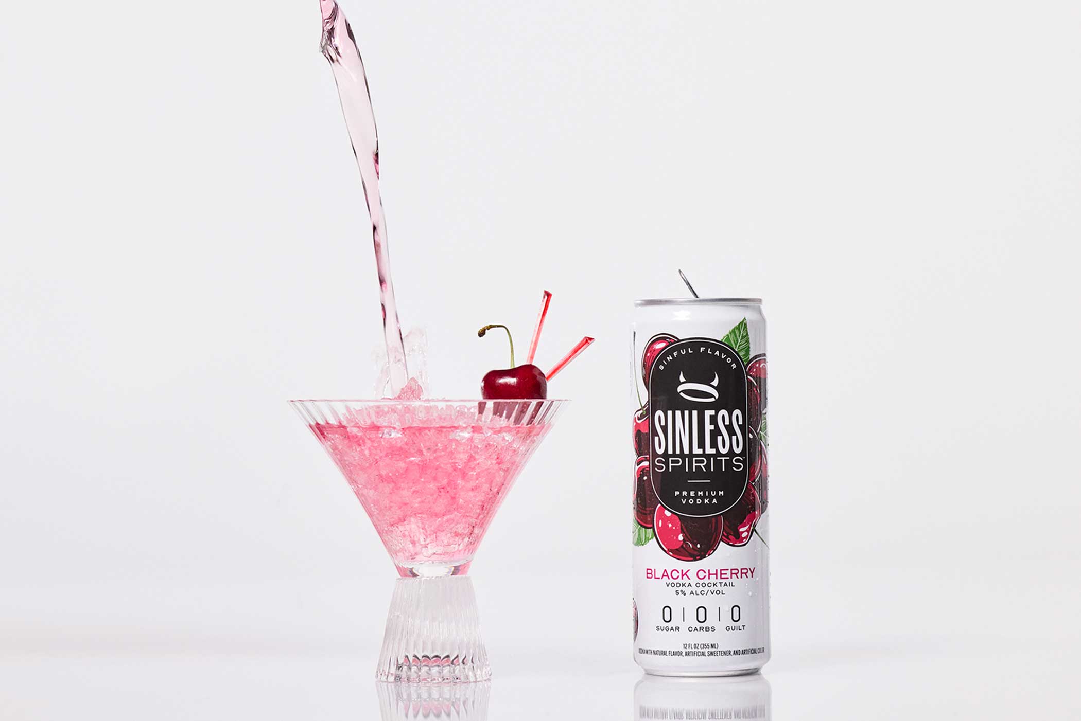 a can of sinless spirits black cherry next to a martini glass being poured into