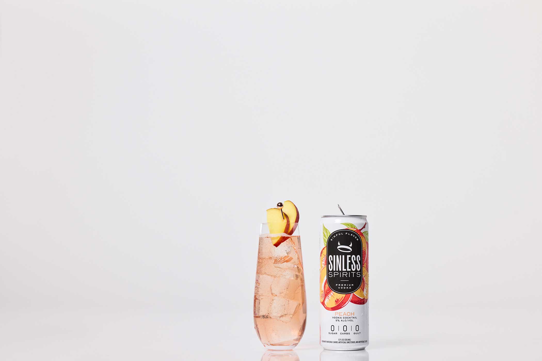a glass filled with sinless spirits peach next to a sinless spirits peach can