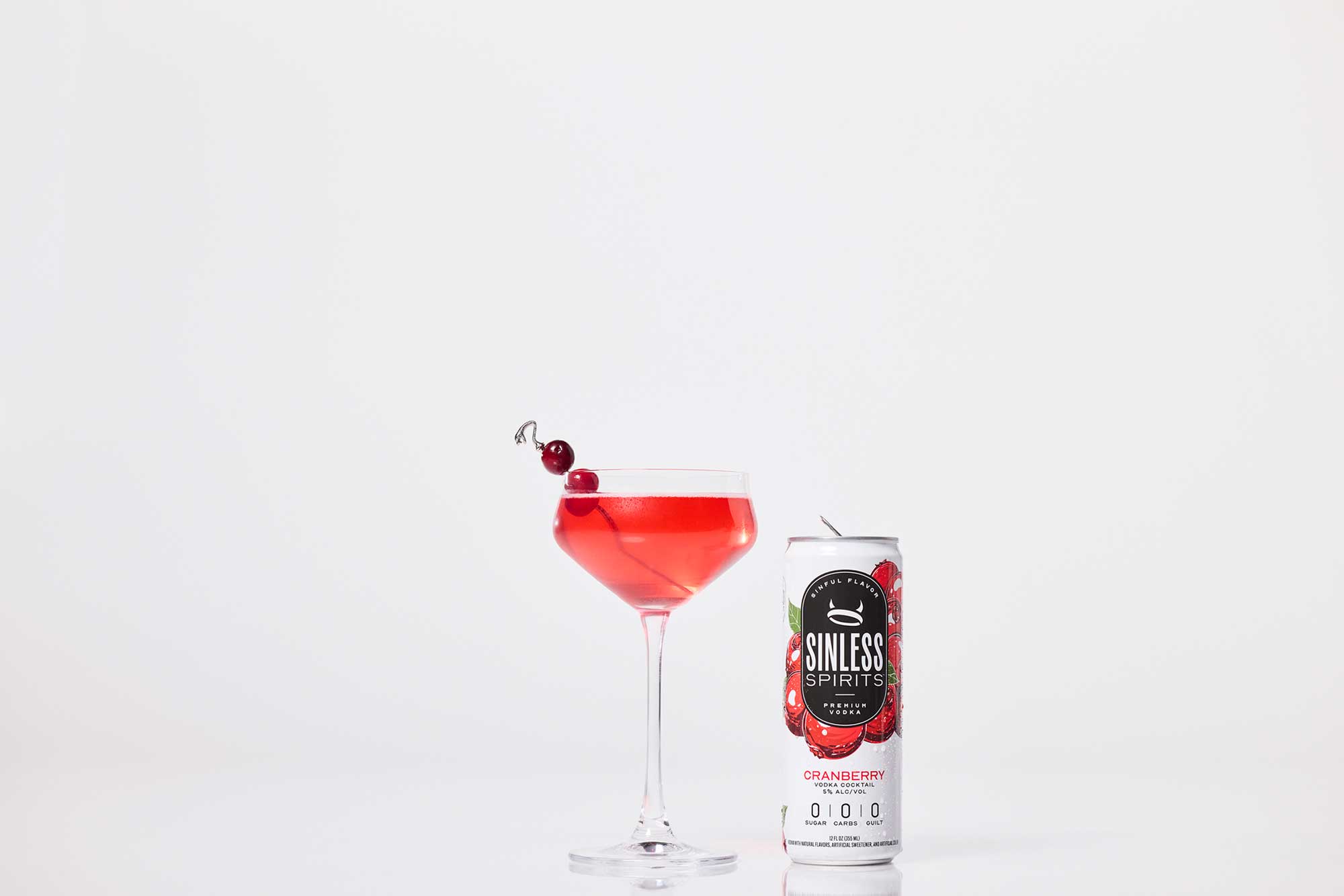 a martini glass filled with sinless spirits cranberry next to a sinless spirits cranberry can